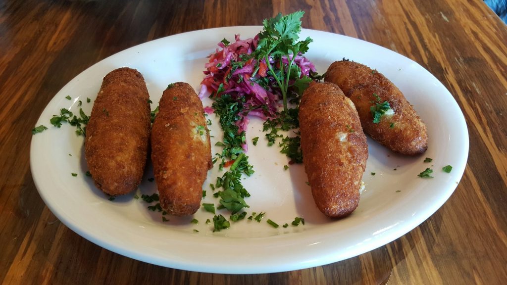 Quatre croquettes dorées sur une assiette ovale, avec du persil et du chou rouge.