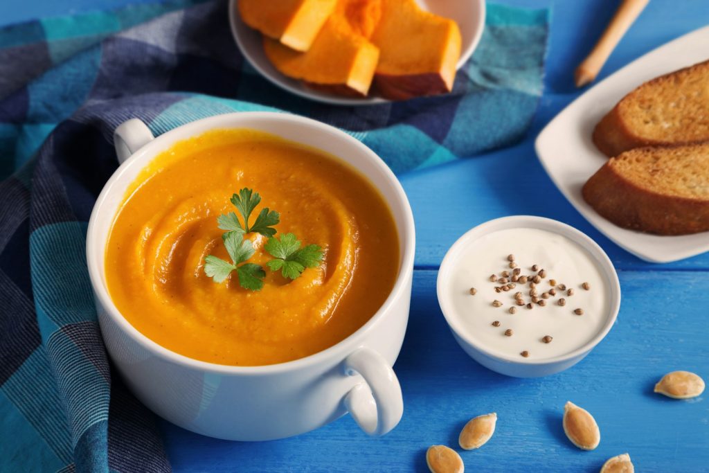 Un velouté de potiron servi dans une tasse, avec des morceaux de potiron et du pain grillé.