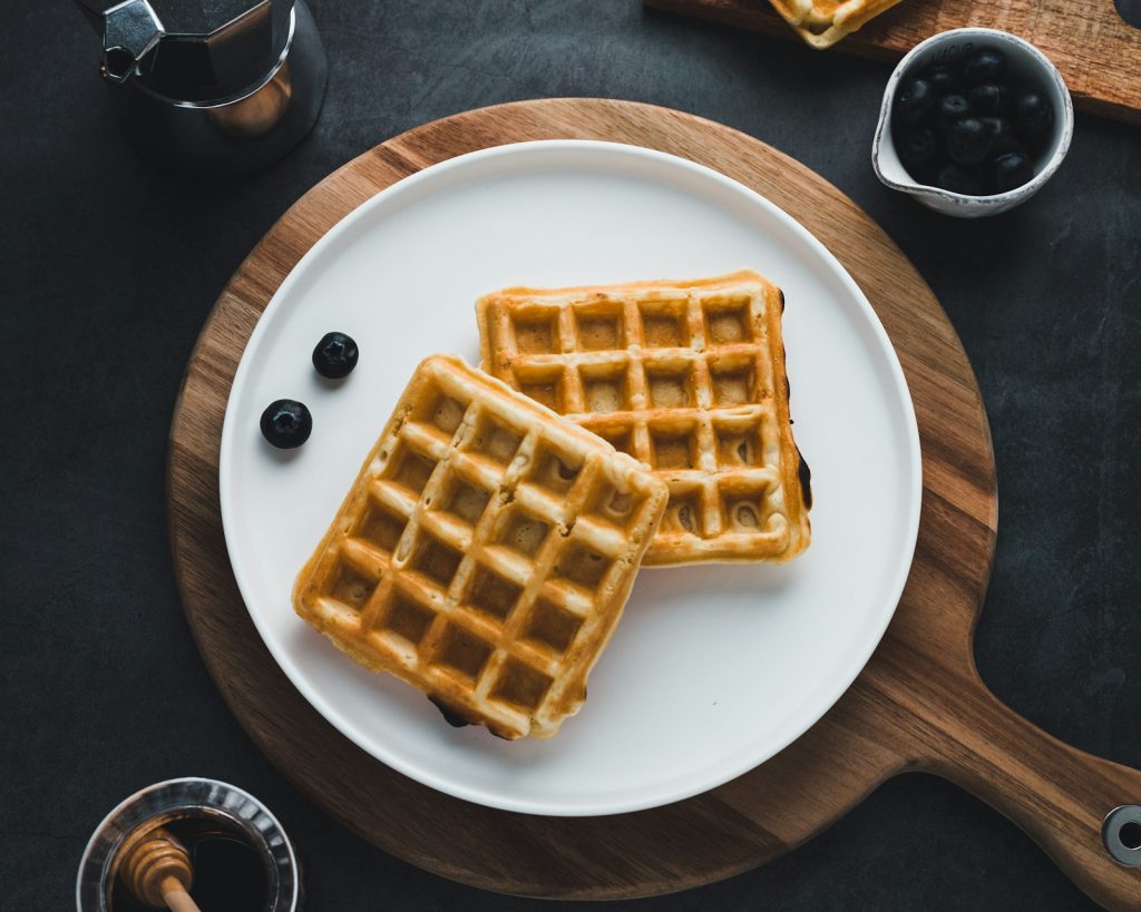 Deux gaufres rectangulaires sur une assiette blanche, avec quelques myrtilles.